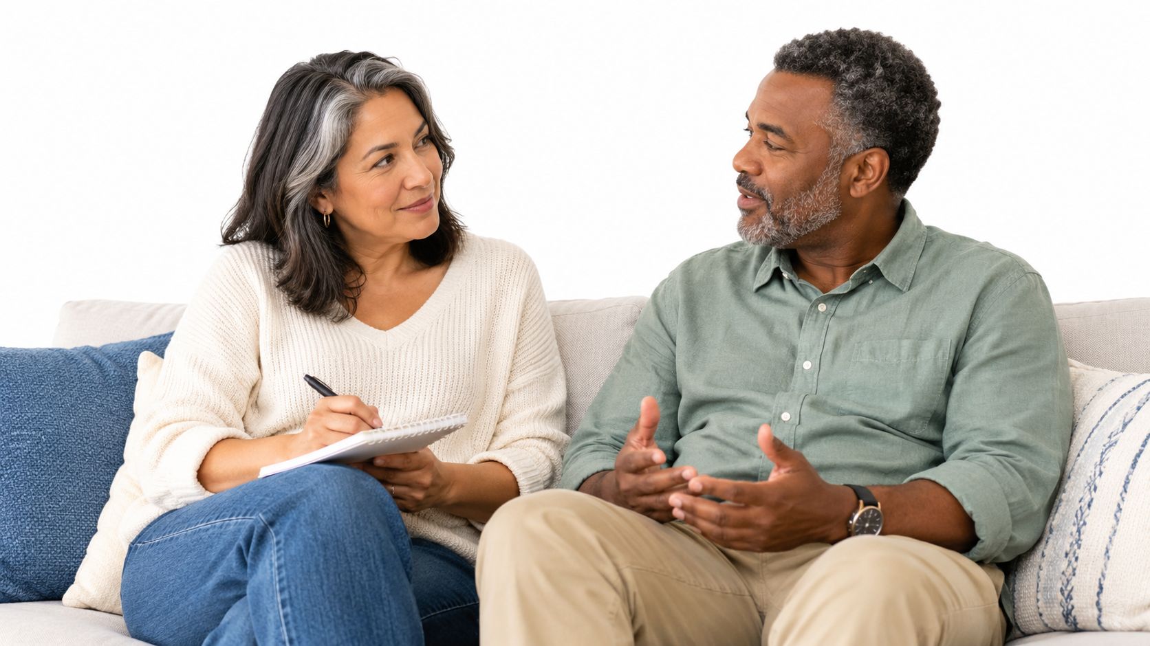 A middle-aged couple sitting on a sofa while having a serious discussion with a notebook and pen.