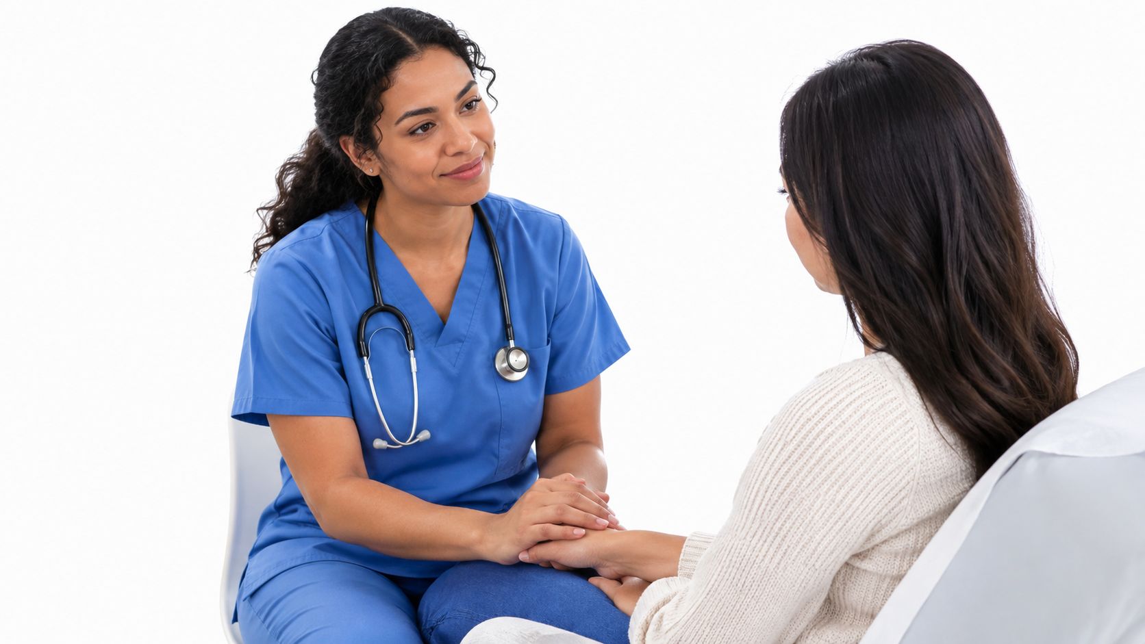 A kind female nurse in blue scrubs holds a patient's hand to provide comfort and care.