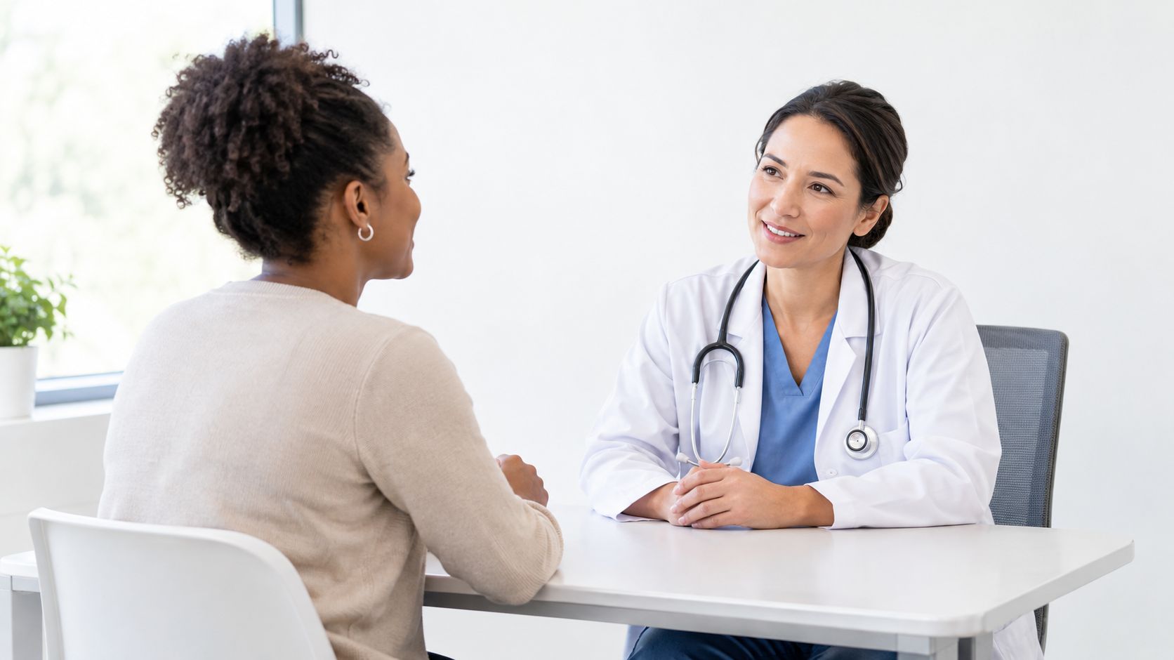 A female doctor with a stethoscope sits at a desk discussing treatment with her female patient.